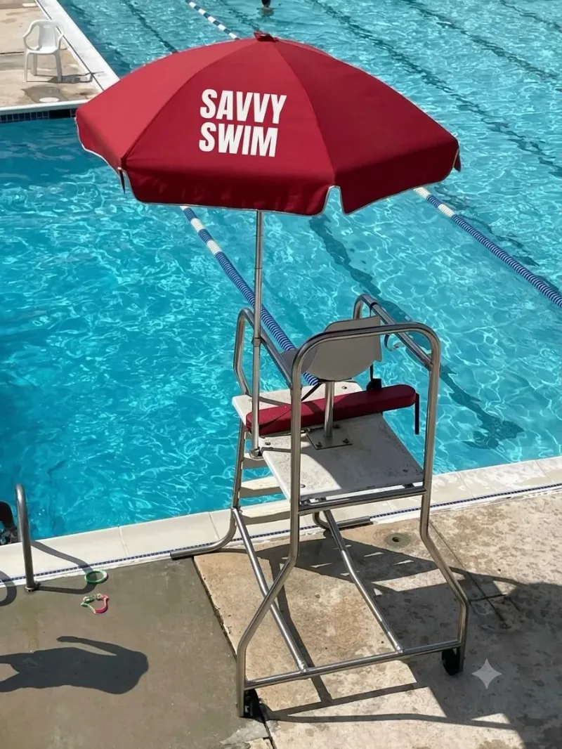 Savvy Swim lifeguard chair under a red Savvy Swim umbrella at a clear pool